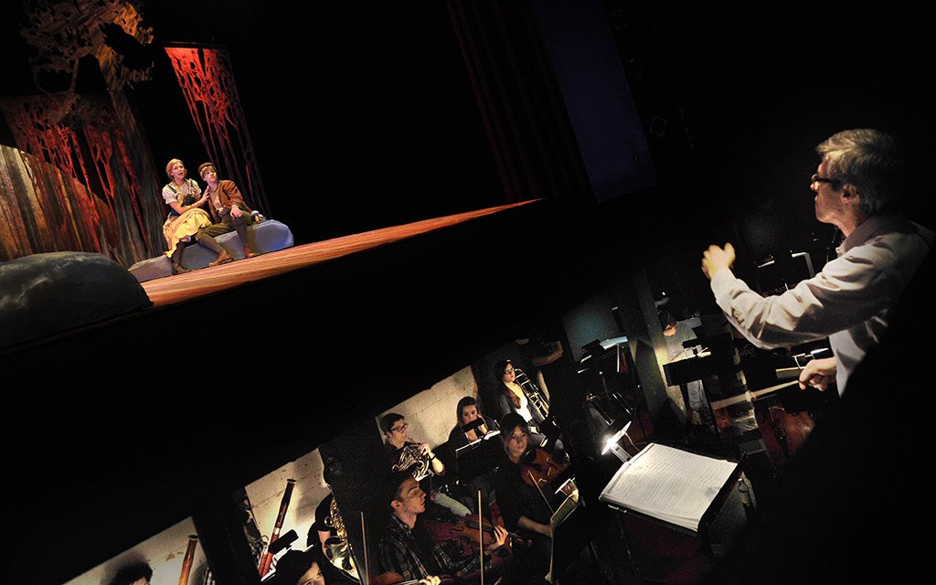 Music theater student perform while orchestra plays soundtrack in bit underneath stage
